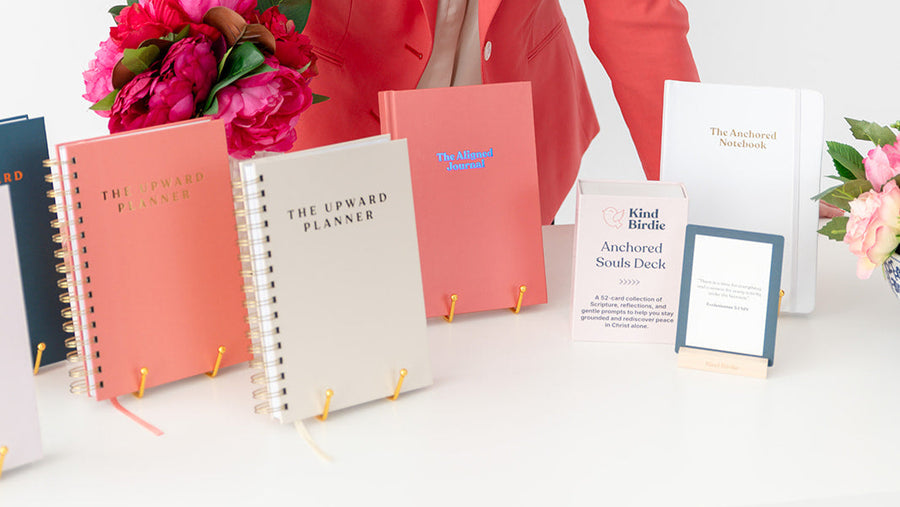 Woman in a coral blazer standing behind a table with planners and flowers.