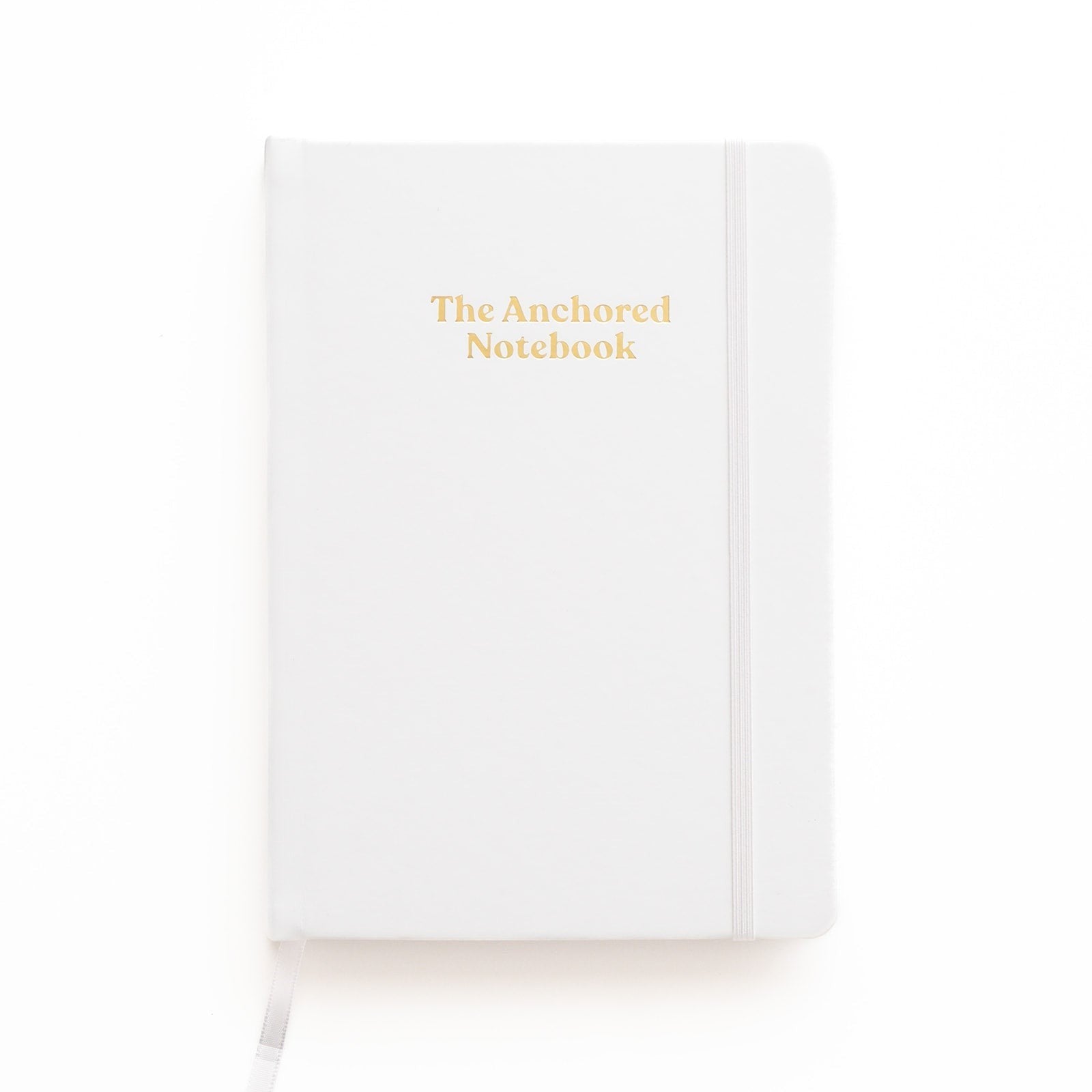 Kind Birdie The Anchored Notebook, a white blank journal with gold lettering and an elastic band closure.