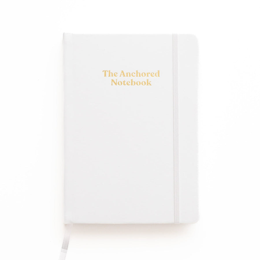 Kind Birdie The Anchored Notebook, a white blank journal with gold lettering and an elastic band closure.
