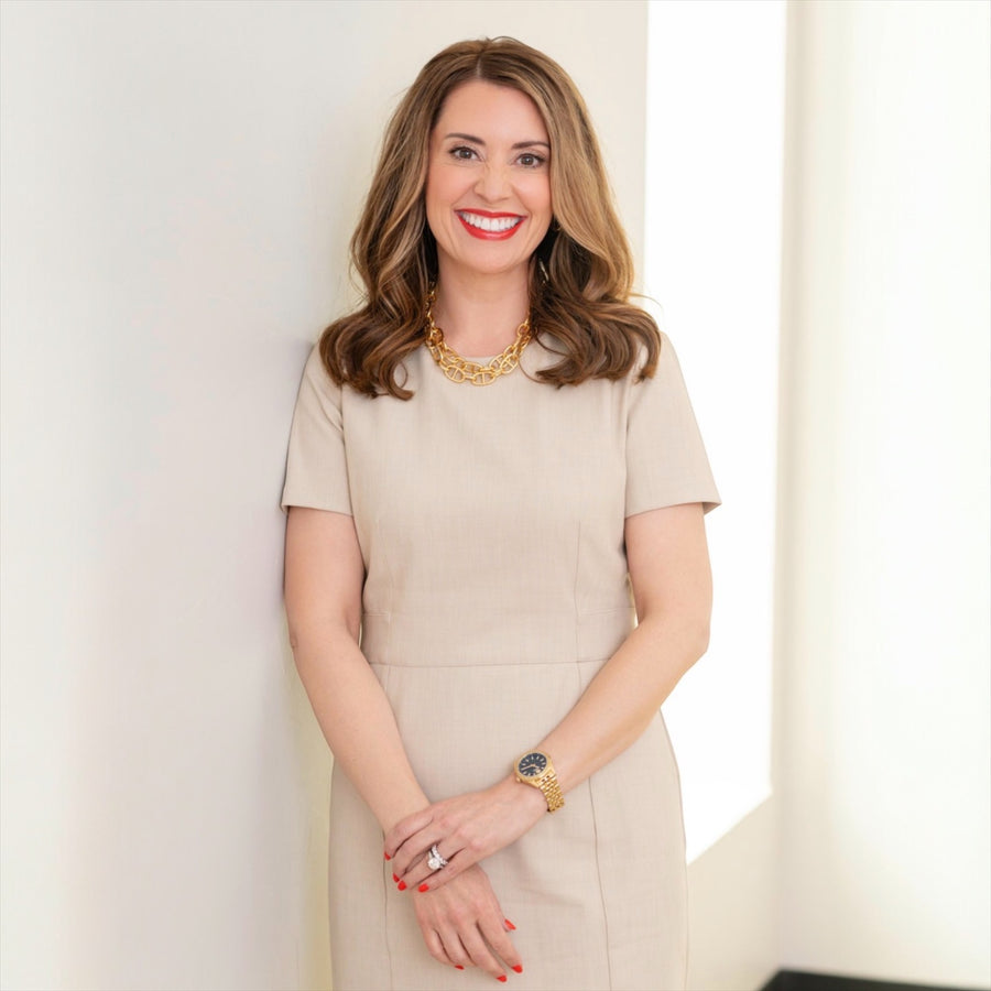 Kind Birdie coach Dana in a beige dress, gold necklace, and watch, smiling. Offers Energy Leadership Index assessment.